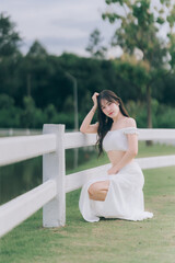 Elegance in the Park: A gracefully poised figure, adorned in pristine white attire, rests against a...