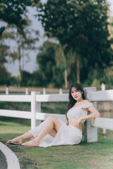 Naklejka premium Serene Portrait in the Park: A young woman finds a moment of peace, leaning against a fence in a park, the sunlight gently caressing her.