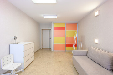 Bright, clean room with a gray sofa, white dresser, chair, and colorful sliding door wardrobe