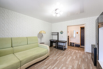 cozy living room with a green sofa, patterned wallpaper, a desk, and a glimpse into a hallway....