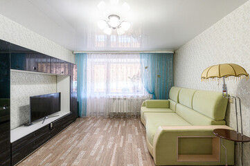 cozy living room with a green sofa, dark TV cabinet, and blue curtains. A quirky umbrella lamp...