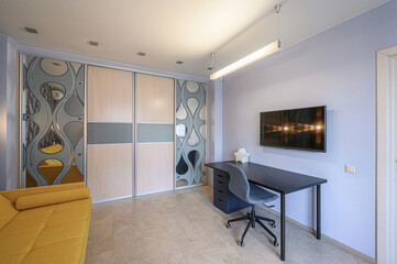 cozy room with a yellow sofa, large closet with decorative panels, a dark desk with a gray chair, and a TV mounted on a light purple wall