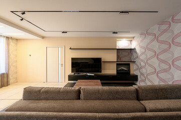 Modern living room featuring a large brown sofa, TV on a black console, and patterned wallpaper. ...