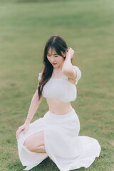 Serene Beauty Amidst Green: A woman kneels gracefully in a lush green field, embodying a tranquil...
