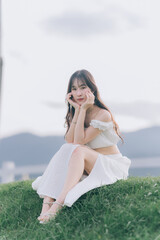 Serene contemplation amidst greenery: A young person with long hair sits gracefully on a grassy hill, enveloped by a soft, natural light, capturing the essence of peace and tranquility.