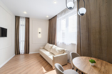 Cozy living room with a beige sofa, wooden floor, curtains, a round table, and a TV on the wall