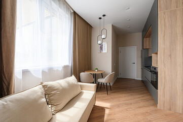 Cozy, modern apartment with a beige sofa, round table with chairs, light fixtures, and a functional kitchen