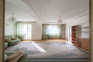 spacious living room is shown with a large patterned rug, green sofas, a wooden floor, and windows...