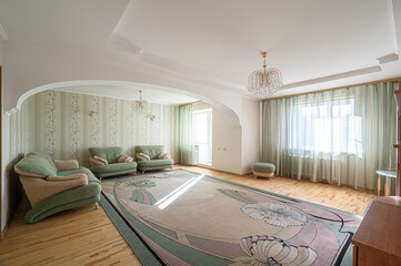 elegant living room with green sofas, a large floral rug, chandeliers, and light green striped...