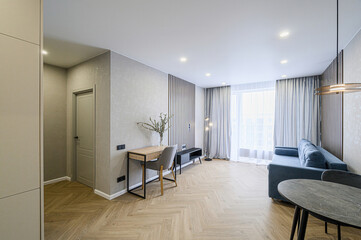 Modern apartment interior with herringbone wood floors, blue sofa, grey accents, desk, and ample...