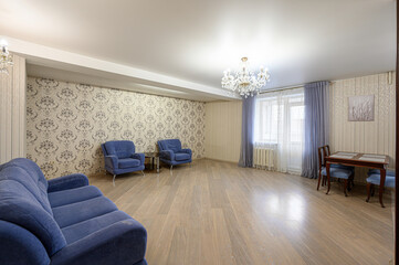 bright living room features blue furniture, patterned wallpaper, a chandelier, and hardwood floors