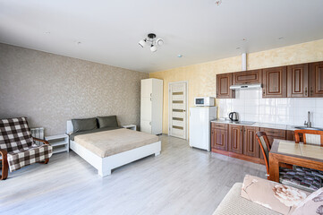 bright studio apartment featuring a bed, kitchen, and sitting area. The design is functional and compact