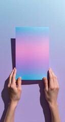 Hands holding a gradient-colored sheet of paper against a pastel background