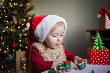 the child sits at the table and dreams or asks on the background of a Christmas tree with lights. Kid's thoughts