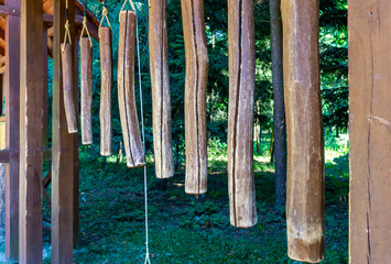 Obraz premium Hanging wooden logs under a garden wooden structure, natural decorative outdoor element, suspended timber pieces on ropes, forest and greenery in the background