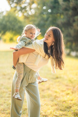 Mother and funny little daughter having fun together in autumn park at sunset light of Prague,...