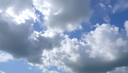 Fototapeta premium A vibrant sky filled with fluffy white clouds and patches of brilliant blue, showcasing the sun's light filtering through the clouds.