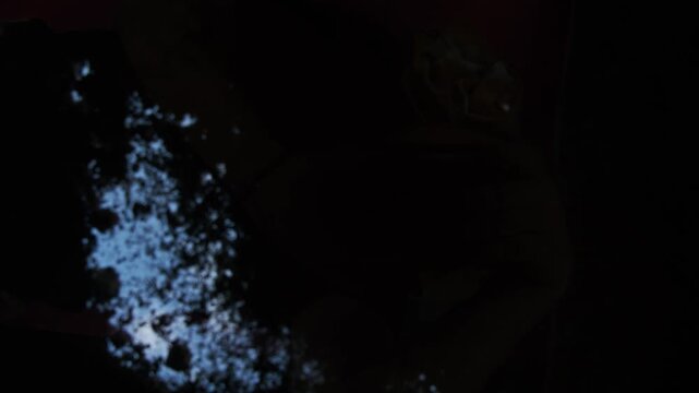 In a freshly dug grave, the gravedigger, or murderer, uses a shovel to fill in the earth, burying the dead man. Low angle. POV. Slow motion.