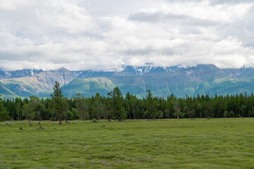 Mountain valley with lush green grass surrounded by mountain ranges covered with clouds