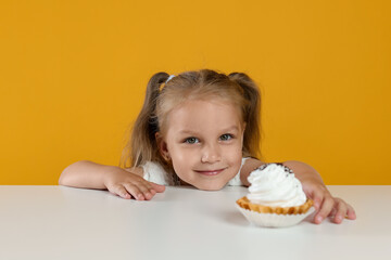 Cute little girl reaching for tasty dessert at white table against orange background