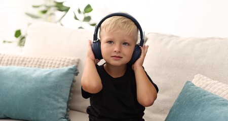 Cute little boy in headphones on sofa at home
