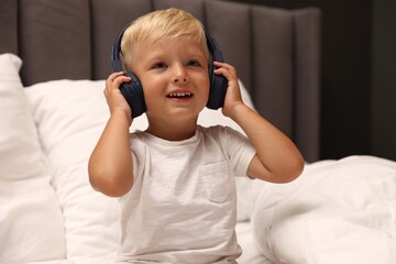 Cute little boy in headphones on bed