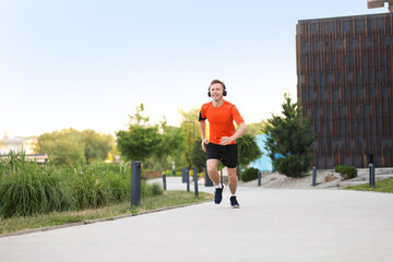 Smiling sportsman in headphones with armband running outdoors, low angle view. Morning exercise