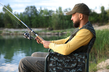 Fisherman with rod sitting on chair and fishing near lake at summer