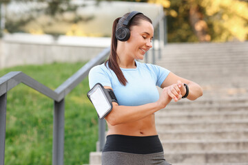 Athletic young woman with headphones checking fitness tracker before running outdoors