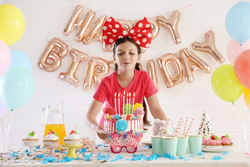 Birthday celebration. Cute little girl blowing out candles on cake and different treats in festive...