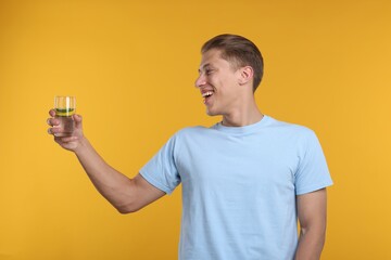 Happy man with glass of refreshing drink on yellow background