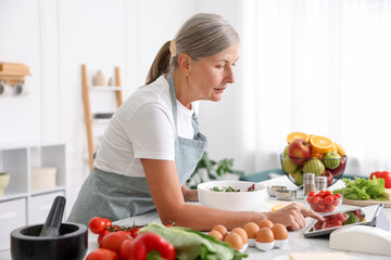 Senior woman using tablet while cooking salad at white marble table in kitchen