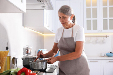 Senior woman cooking dish on cooktop in kitchen