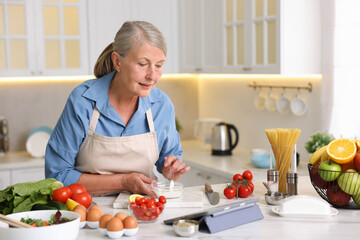 Senior woman using tablet while cooking at white marble table in kitchen