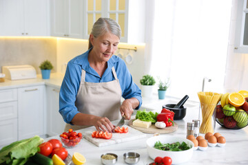 Senior woman cooking at white marble table in kitchen