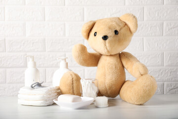 Many different baby accessories and toy bear on table near brick wall