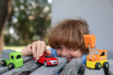 Little boy playing with toy cars on wooden bench outdoors, selective focus
