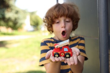 Surprised little boy with toy car outdoors, selective focus