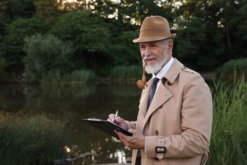 Forensic expertise. Detective with smoking pipe and clipboard working at crime scene near lake...