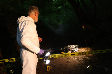 Forensic expert with camera working at crime scene with dead body outdoors, selective focus