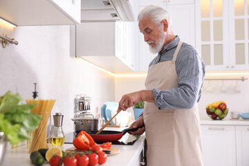 Elderly man cooking dish on cooktop in kitchen
