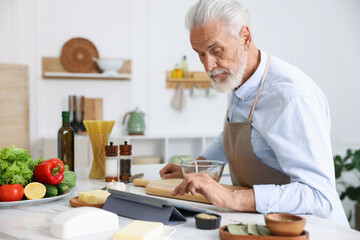 Elderly man using tablet while cooking at white marble table in kitchen