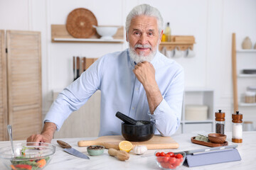 Elderly man cooking at white marble table in kitchen