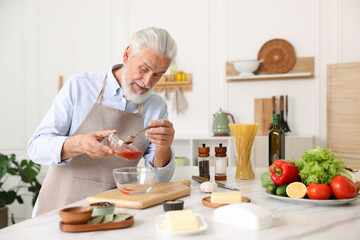 Elderly man cooking at white marble table in kitchen