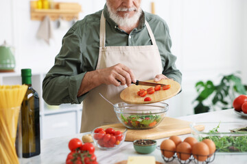 Elderly man cooking salad at white marble table in kitchen, closeup