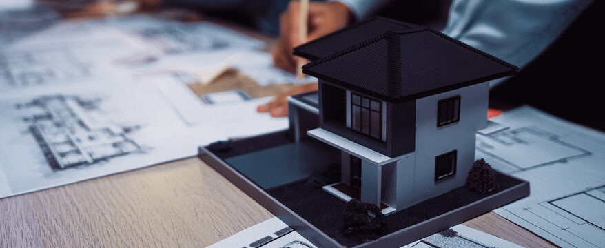 An architectural model sits on a table amid blueprints as designers engage in collaboration. The image captures modern design concepts and teamwork in building projects. SACTR