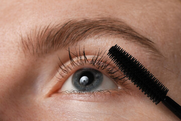 Obraz premium Young woman applying mascara onto her eyelashes, closeup