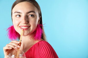 Woman drinking refreshing drink through straw on light blue background, space for text