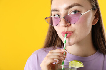 Woman drinking refreshing drink through straw on orange background, space for text