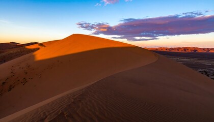 Fototapeta premium A stunning landscape of a vast, reddish-orange sand dune at sunrise, showcasing dramatic shadows and a vibrant sky.